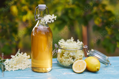 Bottle of elderflower syrup and elderberry flowers on wooden table