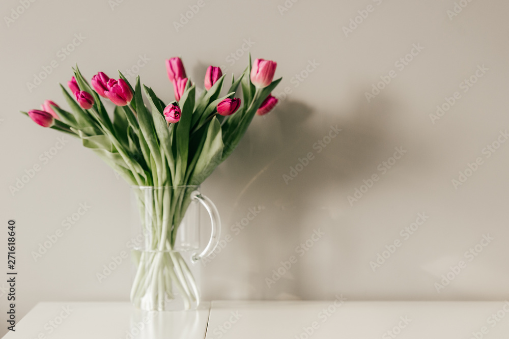 Fototapeta premium Glass vase with bouquet of beautiful tulips on grey wall background.