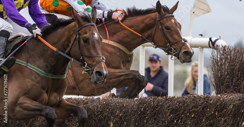 Close up on two competing Race horses and jockeys jumping a hurdle during a race photo