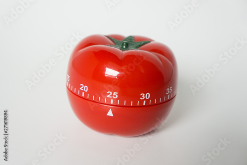 Close up view of mechanical tomato shaped kitchen clock timer for cooking & studying. Used for pomodoro technique for time and productivity management. Isolated on white background, set at 25 minutes.