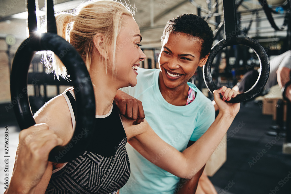 Obraz premium Laughing female friends working out with rings at the gym