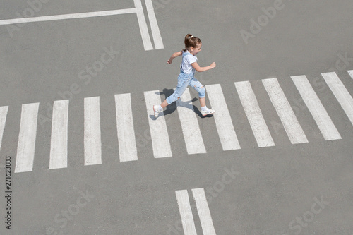 In the summer on the street at the pedestrian crossing kid girl in fashion clothes cross the road. From top view. Shadow at zebra crossing