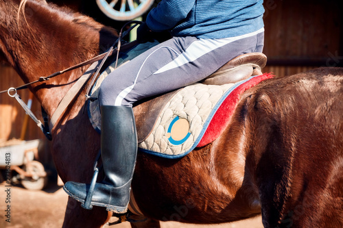 Legs of a rider sitting on the horse saddle at the farm