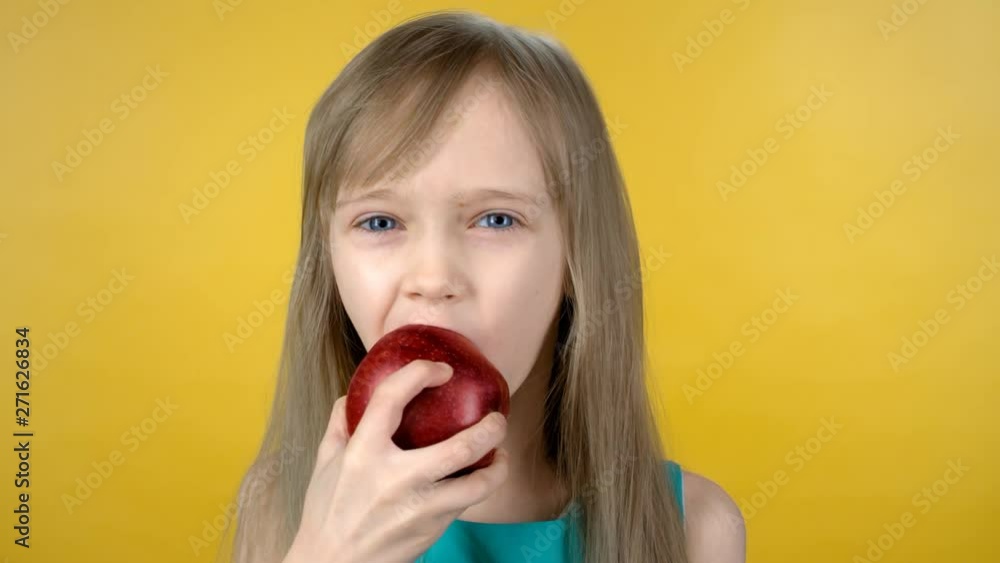 Sequence of portrait shot of boy in glasses and little girl standing isolated on yellow background and biting red apple, then chewing and looking at camera Sequence of portrait shot of boy in glasses and little girl standing isolated on yellow background and biting red apple, then chewing and looking at camera