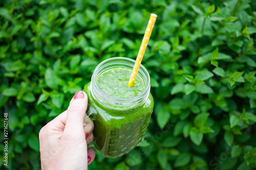 woman's hand holding jar with green cold-pressed juice, vegetable garden background. Healthy eating, detoxing, juicing, body cleancing concept photo