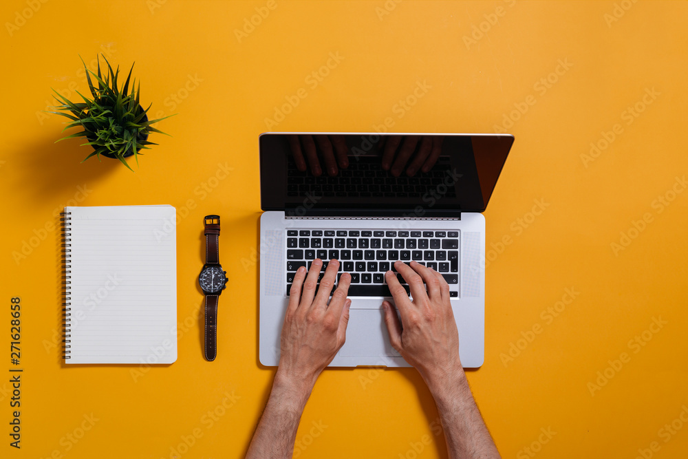 Fototapeta premium flat lay of laptop and notebook on yellow background. male hands typing on keyboard
