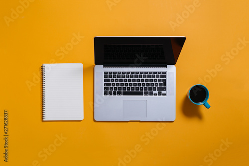 flat lay of laptop, coffee and notebook on yellow background