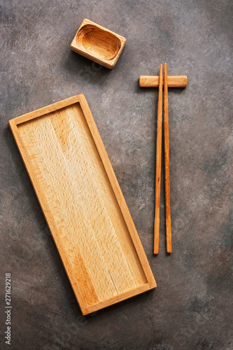 A wooden set of dishes and cutlery Asian cuisine sushi and rolls, a rectangular plate, chopsticks and a bowl for soy sauce on a dark background. Top view, flat lay, copy space.