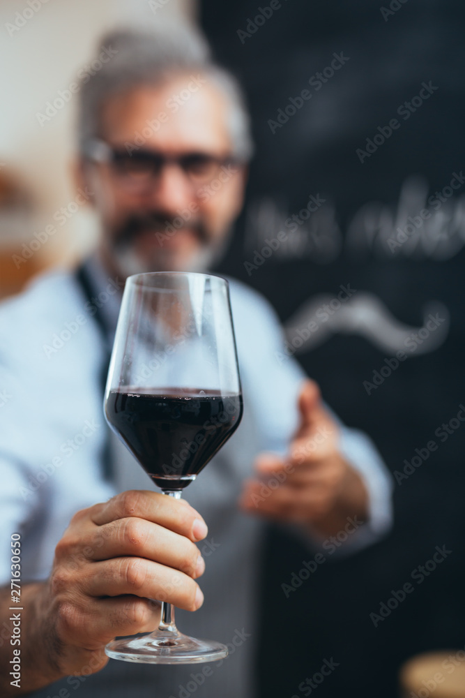 middle aged gray haired bearded man holding glass of red wine in his home kitchen