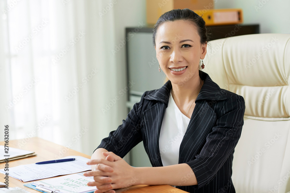 Portrait of young Asian businesswoman sitting at her workplace working with documents and smiling at camera at office Portrait of young Asian businesswoman sitting at her workplace working with documents and smiling at camera at office