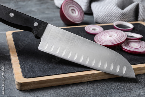 Board with sharp knife and cut onion on grey background photo