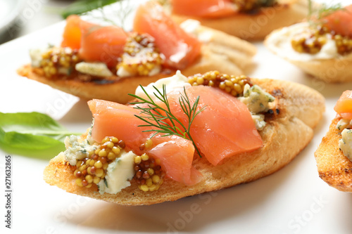 Tasty bruschettas with salmon and blue cheese on plate, closeup