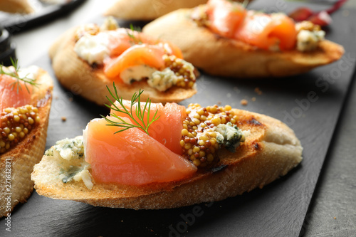 Tasty bruschettas with salmon and blue cheese on slate plate, closeup