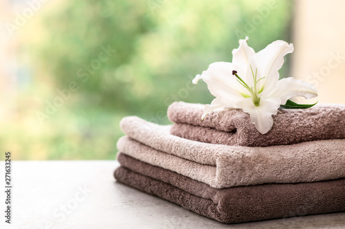 Stack of clean towels with lily on table against blurred background. Space for text