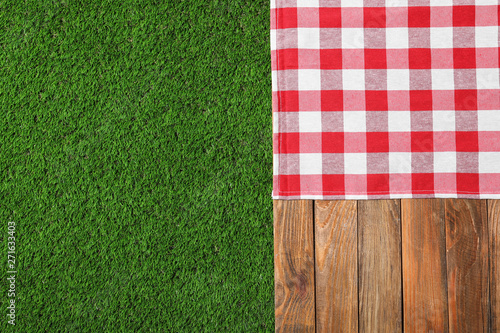 Fototapeta Naklejka Na Ścianę i Meble -  Picnic table with checkered cloth on grass, top view. Space for text