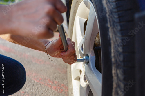 Closeup young woman's hands with good manicure changes wheel on highway using cylinder key to unscrew damaged car wheel. Woman changes flat wheel after her car breaks down. Concept installation tires