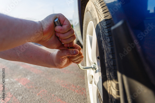 Close-up hands with cylinder wrench unscrew damaged wheel of car. Man changes flat wheel after car breaks down. Wheel balancing, repair and replacement car tires on wheels. Tire installation concept