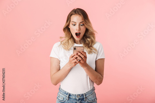 Photos Beautiful shocked young blonde woman posing isolated over pink wall background using mobile phone