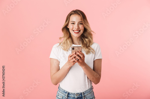 Fotografía Happy young blonde woman posing isolated over pink wall background using mobile phone