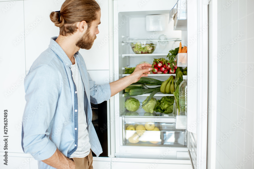 Young vegan man choosing what to cook, taking fresh vegetables from the refrigerator at home Young vegan man choosing what to cook, taking fresh vegetables from the refrigerator at home