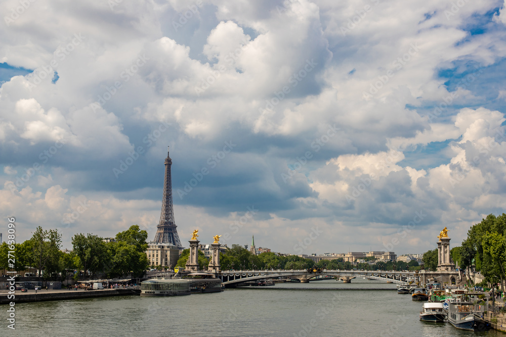View of the Eiffel Tower along the Seine River. Bridge of Alexander the Third in Paris. Bright and cloudy sky.