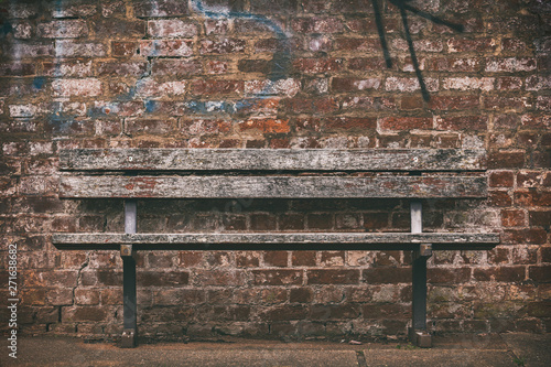 old wooden bench against a brick wall with graffiti.