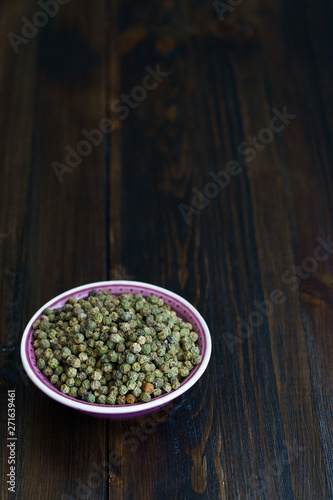 Dried green peppercorns in a violet bowl. Dark wooden table  high resolution  negative space