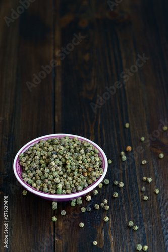 Dried green peppercorns in a violet bowl. Dark wooden table  high resolution  negative space