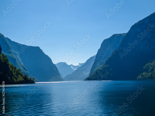 A view on the Songefjorden (King of the Fjords) from the water level. It is the deepest fjord in Norway. Tall, lush green mountains surrounding the fjord. Calm surface of the water. Clear blue sky. © Chris