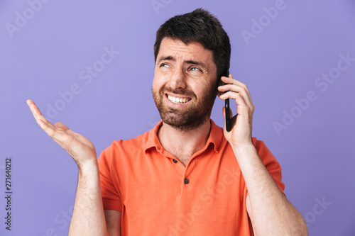 Confused young handsome bearded man posing isolated over violet purple wall background talking by mobile phone.