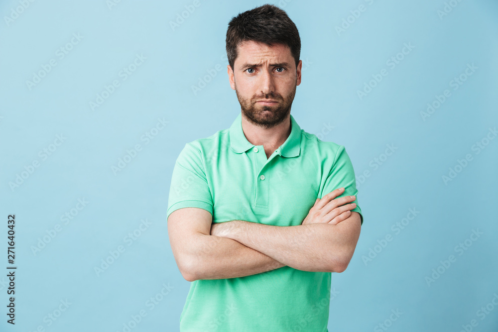 Displeased young handsome bearded man posing isolated over blue wall background. Displeased young handsome bearded man posing isolated over blue wall background.