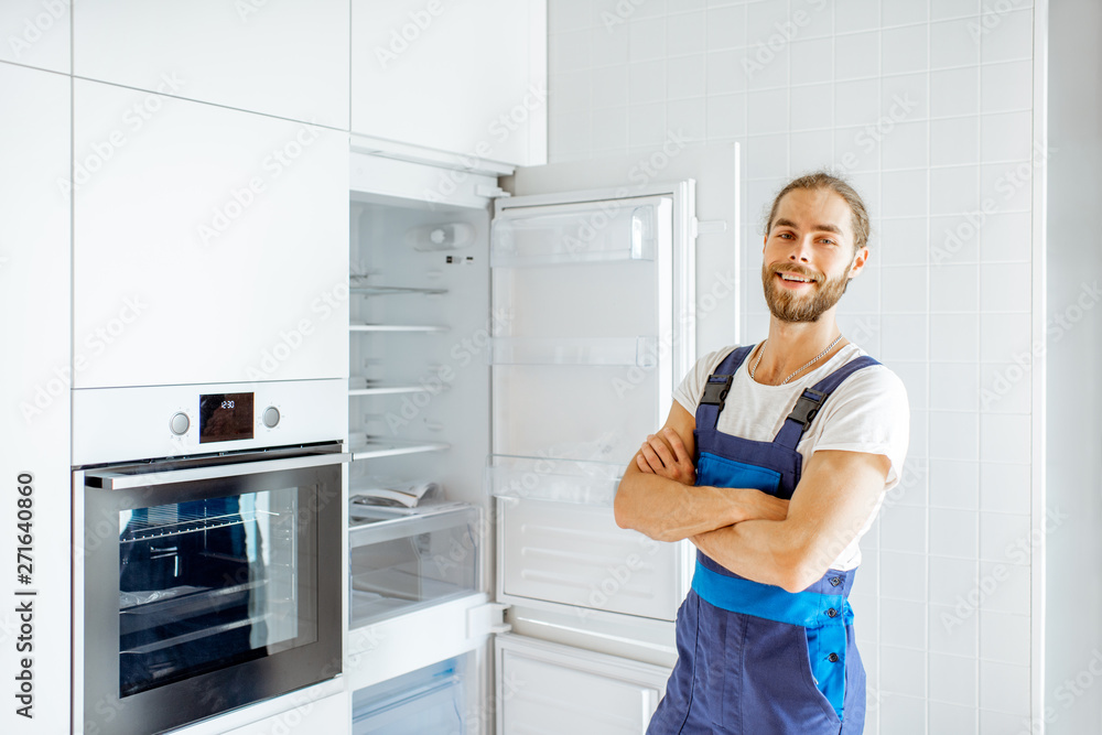 Portrait of a handsome workman installing new refrigerator in the modern kitchen at home Portrait of a handsome workman installing new refrigerator in the modern kitchen at home