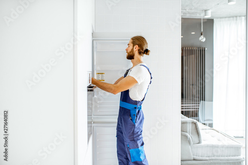 Handsome workman installing new refrigerator in the modern kitchen at home
