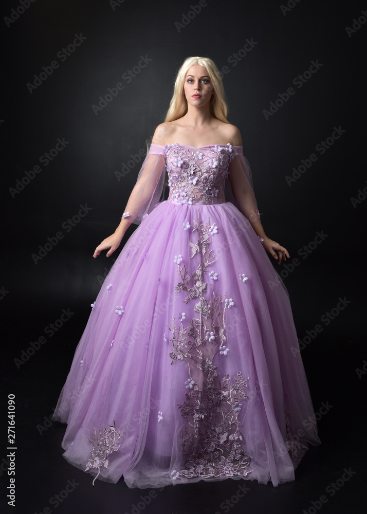 full length portrait of a blonde girl wearing a fantasy fairy inspired costume, long purple ball gown with fairy wings, standing pose on a dark studio background. full length portrait of a blonde girl wearing a fantasy fairy inspired costume, long purple ball gown with fairy wings, standing pose on a dark studio background.