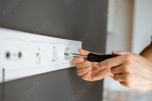 Electrician mounting electric sockets on the grey wall at home