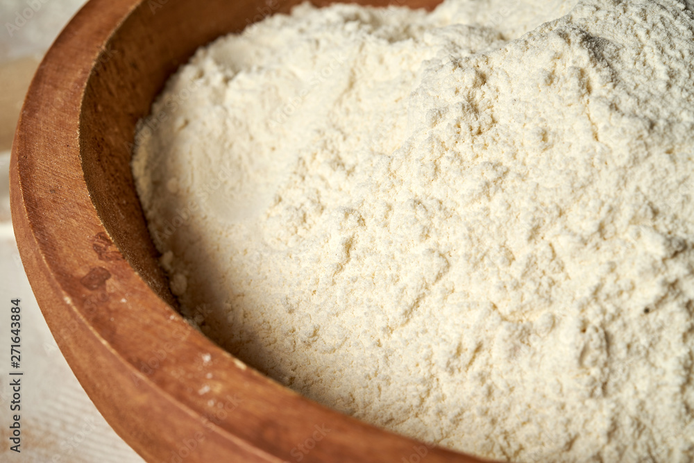 Closeup of flour in wooden bowl on a white table.