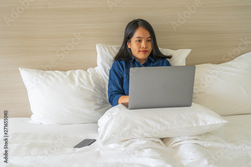Young freelancer woman using laptop on white bed 