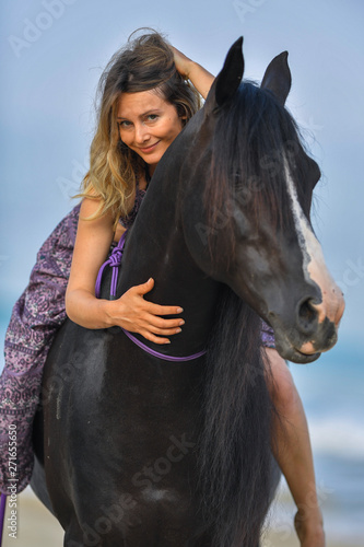 Portrait of a beautiful blond girl run on the sand with her black horse on the Rishpon beach, Israelck horse on the Rishpon beach, Israel © PROMA