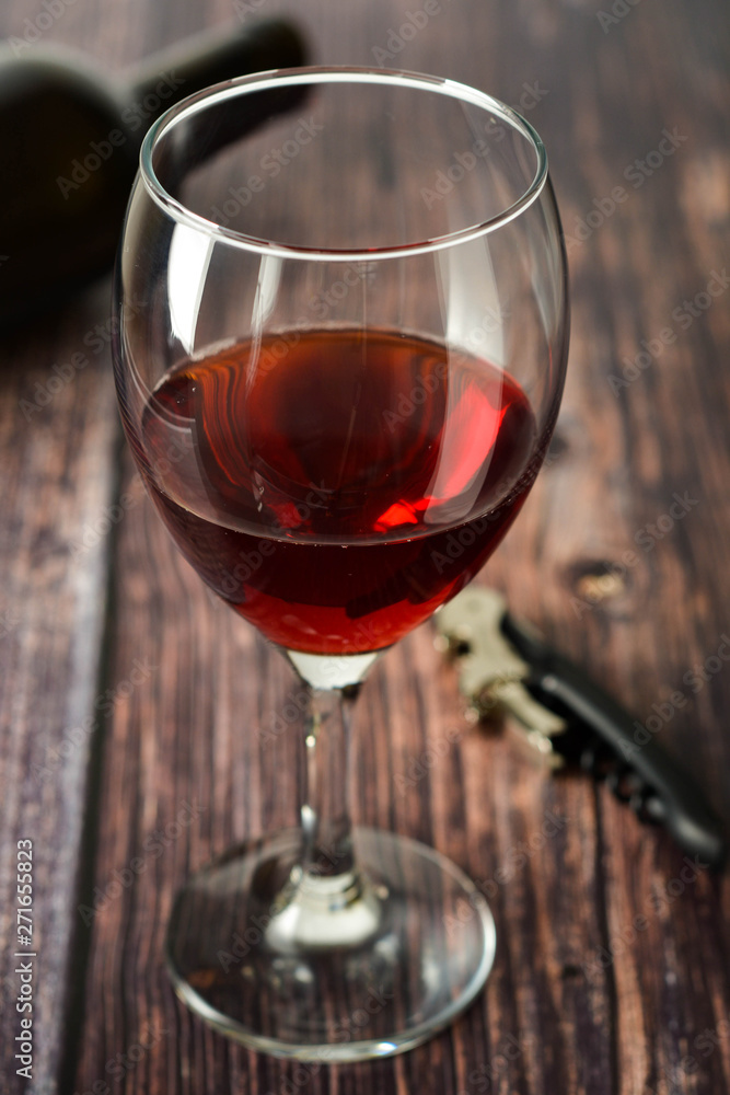 Glass of red wine over rustic, wooden textured table. Dark photo.