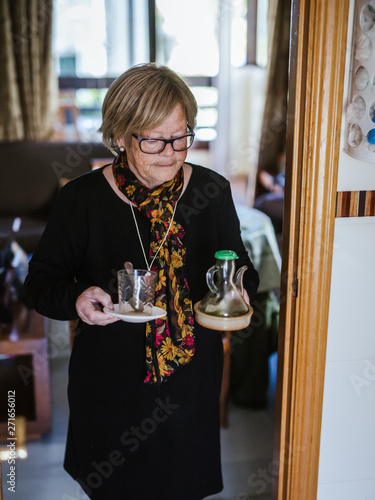 Senior woman holding in hands glass cup and jug while walking around house photo