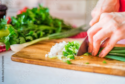 Female hand with knife cuts green leek in kitchen. Cooking vegetables