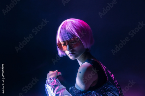 Trendy young Japanese woman with purple hair standing in sparkly silver jacket and red sunglasses sitting on blue background photo