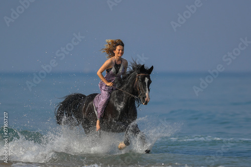 Portrait of a beautiful blond girl galloping on horseback, dissecting waves on the sea beach