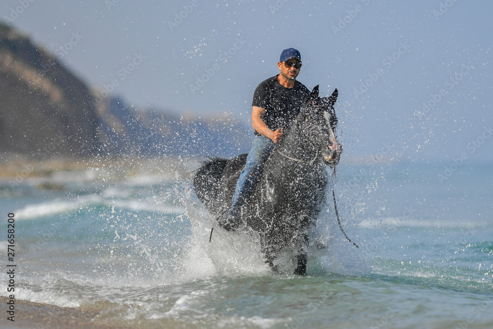 Fototapeta premium Portrait of a man galloping on horseback, dissecting waves on the sea beach