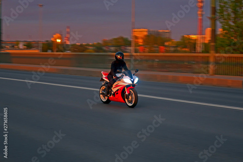 Motorcyclist riding at high speed over the bridge in the evening with headlights on