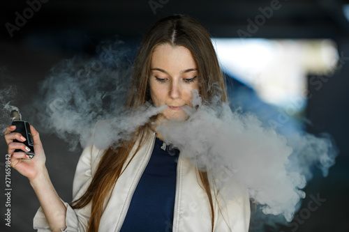 Vape teenager. Young cute girl in  casual clothes smokes an electronic cigarette outdoors in summer day. Bad habit that is harmful to health. Vaping activity. Close up.
