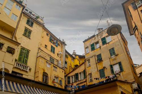 Low angle view of old building exteriors in a narrow alley of the historic centre of Genoa, with yellow façade and green shutters, in a rainy day with overcast sky, Liguria, Italy photo