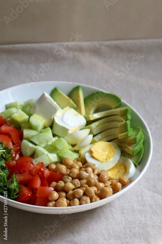 Lunch bowl with avocado, hard boiled egg, chickpea, feta cheese, cucumber, tomato and arugula. Selective focus.