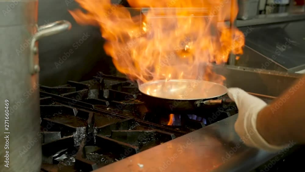 chef flips food in frying pan in professional kitchen. A young chef picks up frying pan on gas stove and mixes and flips vegetables in frying pan. chef flips food in frying pan in professional kitchen. A young chef picks up frying pan on gas stove and mixes and flips vegetables in frying pan.
