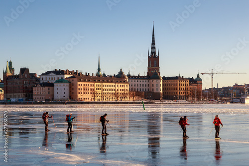 People are ice skating on frozen Riddarfjärden bay of lake Mälaren by Gamla Stan (Old Town) island, on a bright sunny and cold winter day with sub-zero temperature in Stockholm, Sweden.